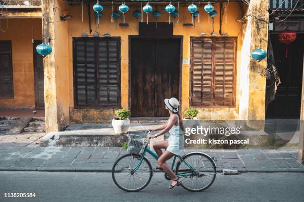 woman tourist cycling in the old district of hoi an in vietnam during day . - vietnam stock-fotos und bilder