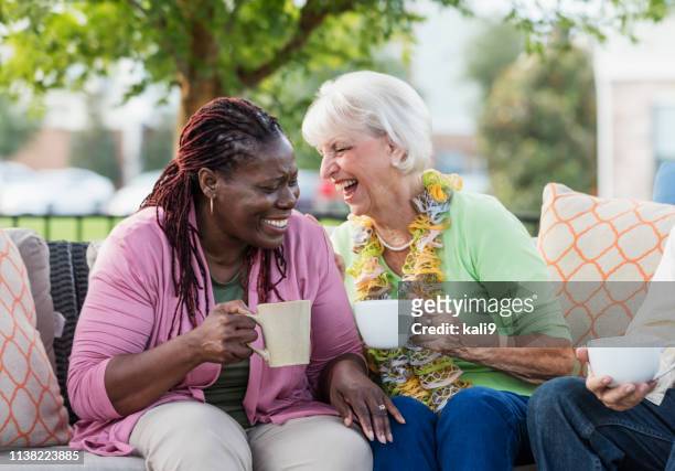 senior woman, african-american friend laughing together - coffee on patio stock pictures, royalty-free photos & images