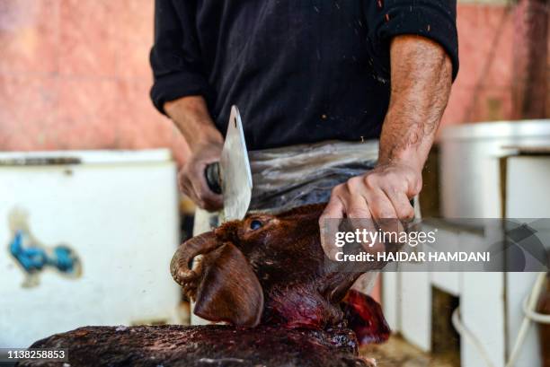 An Iraqi man uses a cleaver to chop a lamb's head while preparing "pacha", a traditional local traditional dish made from slowly-boiled sheep's head,...