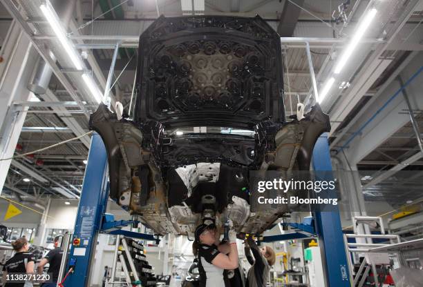 Worker uses a drill underneath a Mercedes-Benz E-Class automobile on the production line at the Daimler AG luxury automobile plant in Moscow, Russia,...