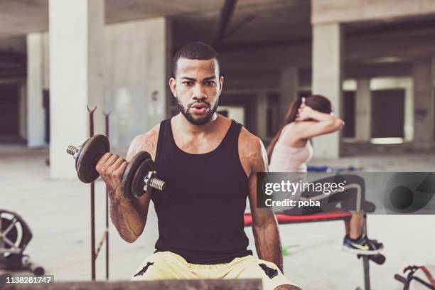 haltère de levage de jeune homme dans une salle de gym urbaine - musculation des biceps photos et images de collection