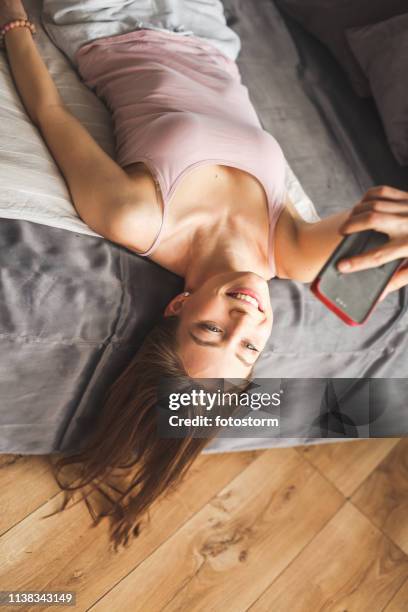 girl lying on back on bed holding mobile above her head - smartphones dangling stock pictures, royalty-free photos & images