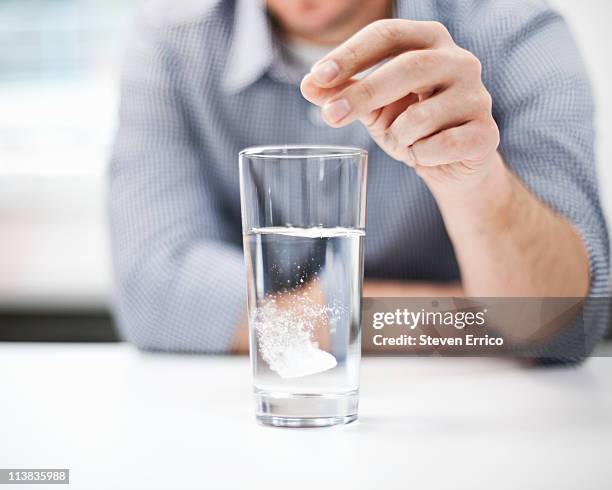man dropping antacid into a glass of water - antiacid fotografías e imágenes de stock
