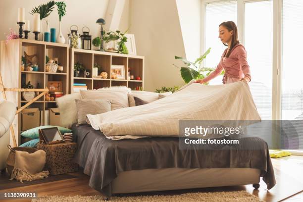giovane donna che fa il letto a casa - spread foto e immagini stock