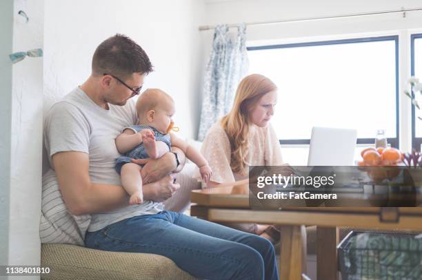 mama arbeitet am computer, während papa hält ihre baby-tochter - gender stereotypes stock-fotos und bilder