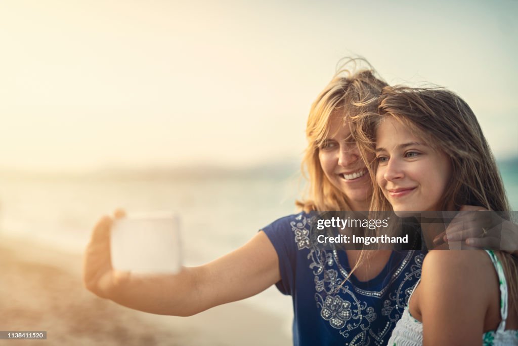 Mother and daughter embracing and taking selfies at the beach