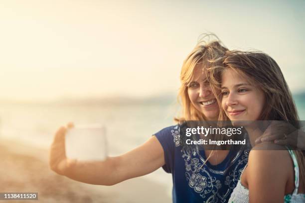 mor och dotter omfamna och ta selfies på stranden - girl beach sunset bildbanksfoton och bilder