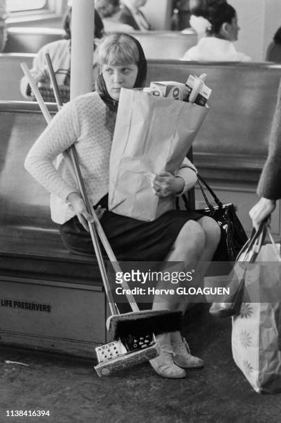 Une femme assise avec un sac de courses et deux balais à state du ferry 'State Island' New York, Etats-Unis.