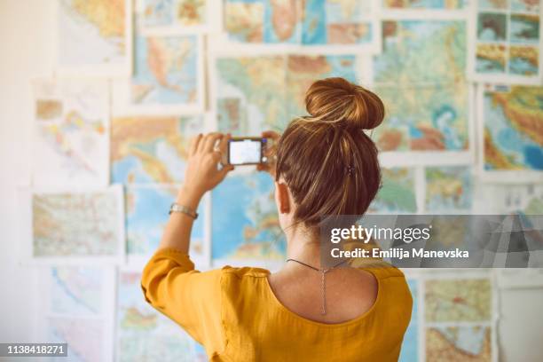 young woman taking photo with mobile phone and looking at world map - world social media day stock pictures, royalty-free photos & images