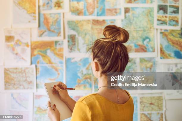 young woman handwriting at notebook while looking at map - guiding fotografías e imágenes de stock