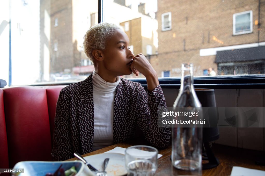 Pensive woman sitting by herself in a restaurant at lunch break