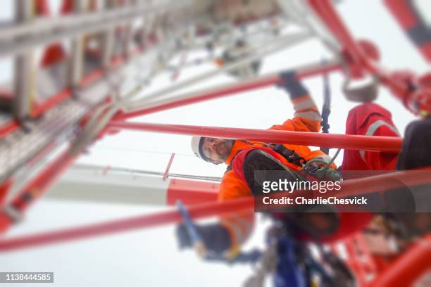 technicien d'accès de corde grimpant sur la tour-antenne avec des crochets et regardant vers le bas - antennes photos et images de collection