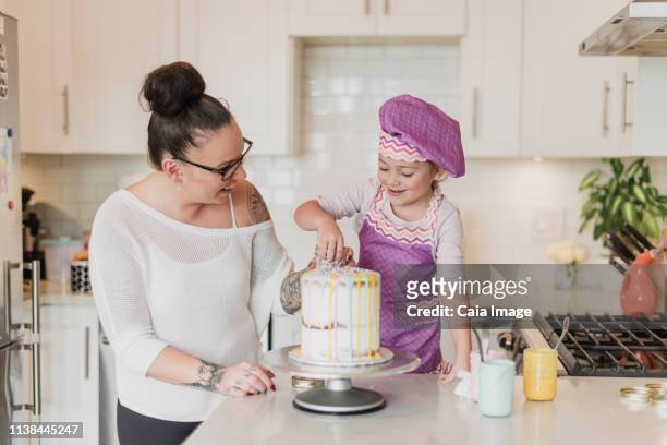 mother and daughter decorating cake in kitchen - gateaux fotografías e imágenes de stock