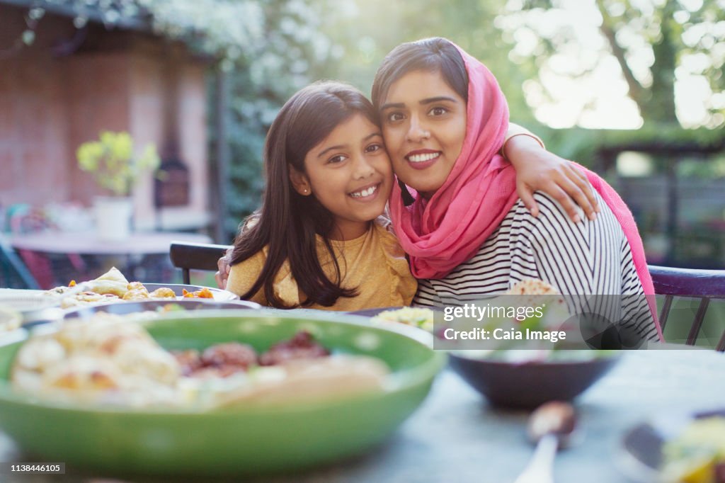 Portrait happy mother in hijab and daughter hugging at dinner table
