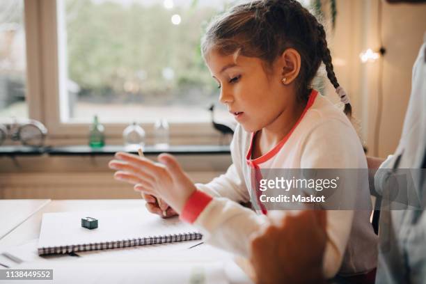 midsection of mother sitting with daughter writing homework on table at home - young girls homework stock pictures, royalty-free photos & images