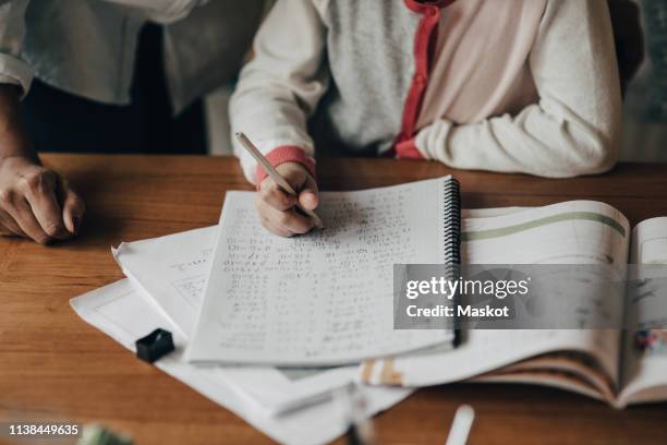 midsection of mother standing by daughter writing homework on table at home - math homework stock pictures, royalty-free photos & images