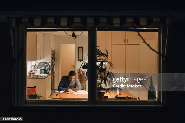 high angle view of boy studying while sitting at home seen through window - attentif photos et images de collection
