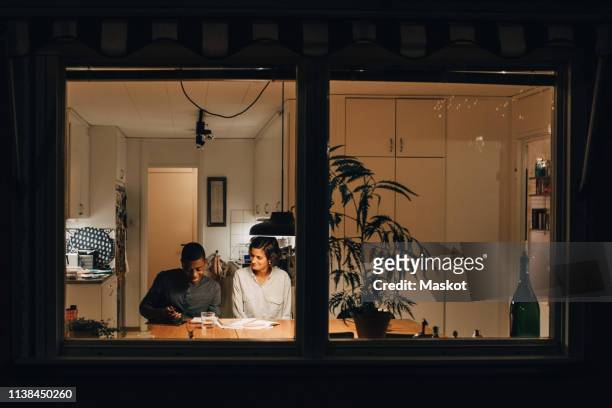 mother assisting son in studying at home seen through window - raam stockfoto's en -beelden