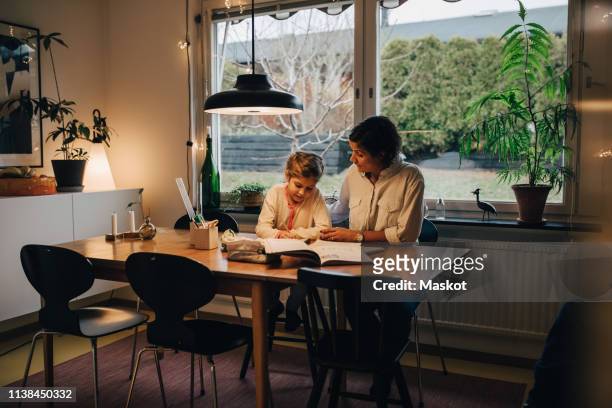 mother assisting daughter in writing homework while sitting at home - homework bildbanksfoton och bilder