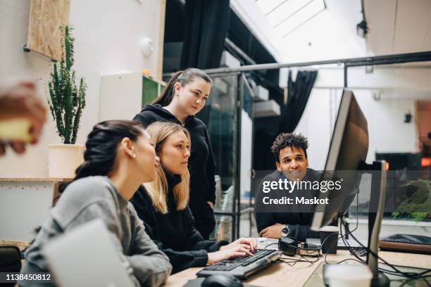 colleagues discussing over computer at desk in office - developer stockfoto's en -beelden