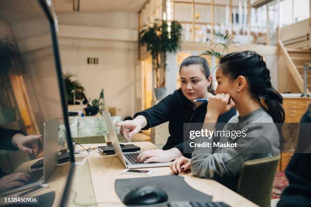 female coworkers discussing coding on laptop while sitting in office - designer profissional fotografías e imágenes de stock