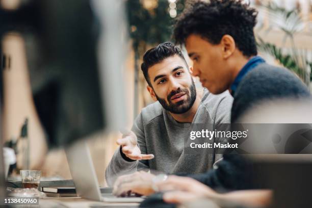 male computer programmers discussing over laptop on desk while sitting in office - it professional imagens e fotografias de stock