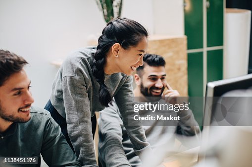 Smiling colleagues looking at computer while working in office Smiling colleagues looking at computer while working in office