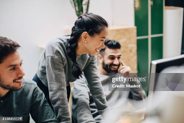 smiling colleagues looking at computer while working in office - young women group stock pictures, royalty-free photos & images