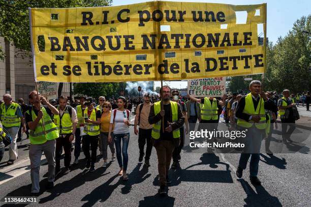 Protesters walk behind a large banner that reads &quot;RIC for a national bank and free themselves from debt&quot; during the Yellow Vests Act 23...