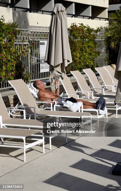 Man reads a magazine as he lounges in the sun beside a hotel swimming pool in Palm Springs, California.