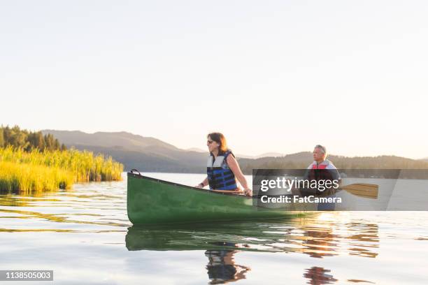 older couple canoe together on a lake at sunset - seniors canoeing stock pictures, royalty-free photos & images