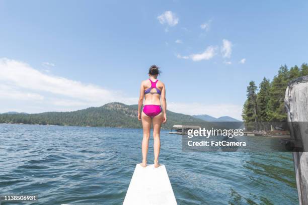 a young woman stands alone at the edge of a diving board over the lake - 2017 usa diving summer stock pictures, royalty-free photos & images