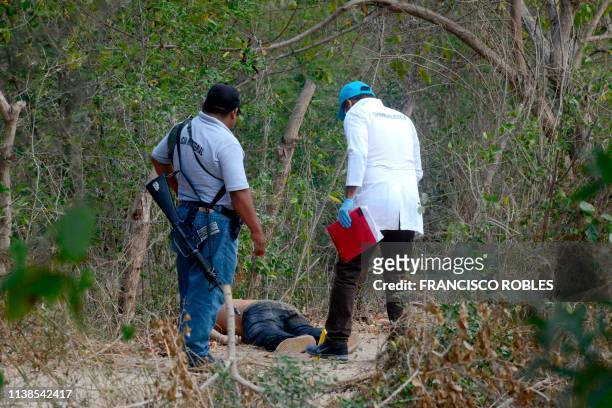 An investigator of the prosecution office and a policeman work at the crime scene next to a man's corpse in the outskirts of Acapulco, Guerrero...