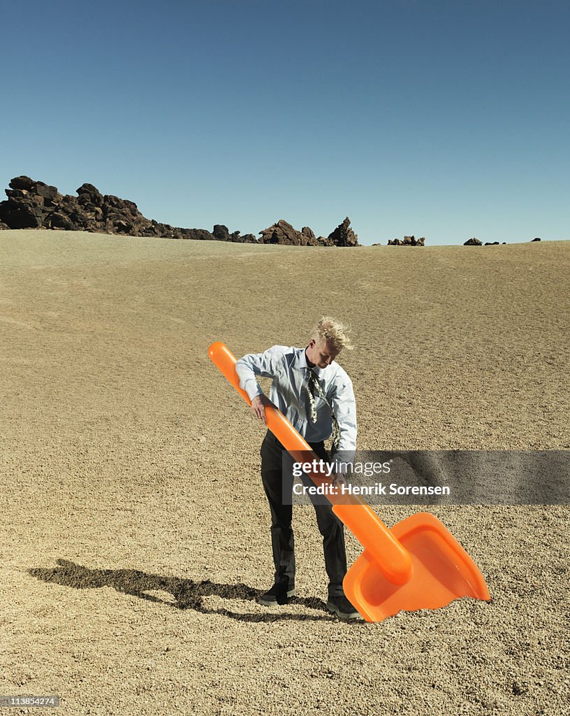Businessman digging with oversized plastic spade