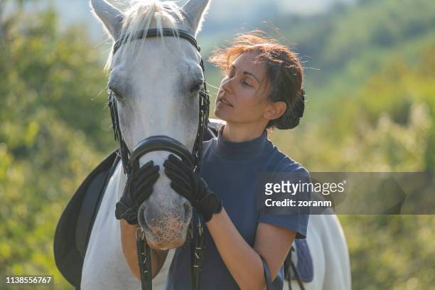 woman holding her mare's snout with affection - racehorse owner stock pictures, royalty-free photos & images