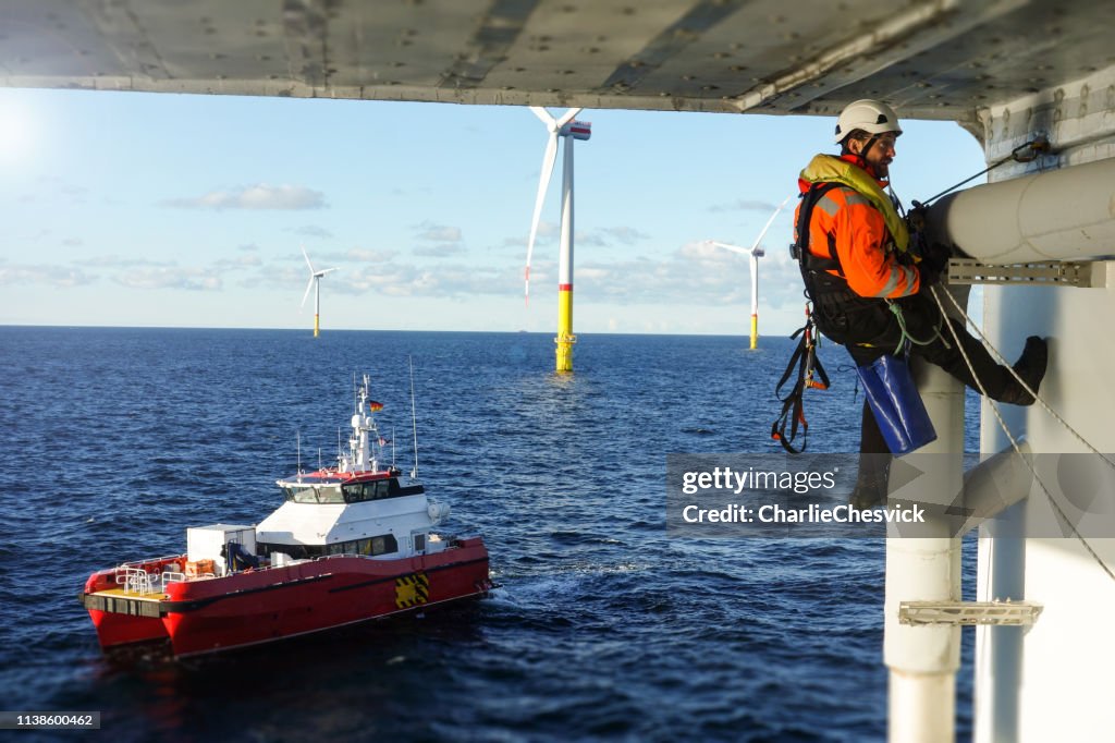 Technicien d'accès de corde effectuant l'inspection, réparant sur la plate-forme offshore avec la protection de navire de transfert