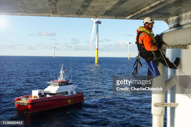 rope access technician making inspection, repairing on offshore platform with transfer vessel guarding - repairing boat stock pictures, royalty-free photos & images