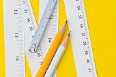 Yellow pencil and white measuring tapes with centimetre and inches on vivid yellow background, length, long or maker instrument and tools concept