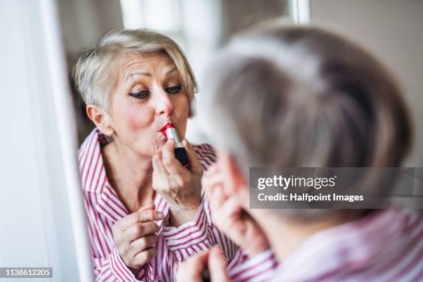 a rear view of active senior woman applying make-up at home, looking in the mirror. - lip liner stock pictures, royalty-free photos & images
