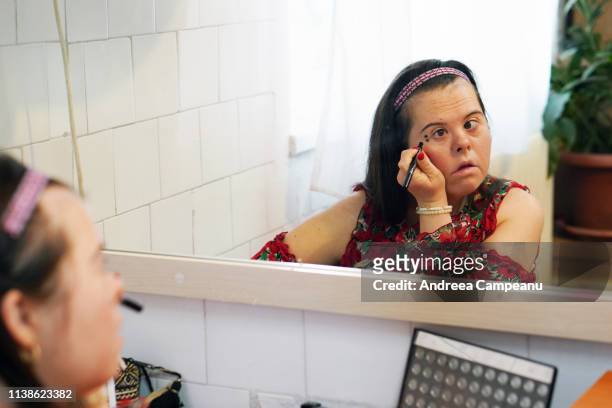 a young woman with down syndrome is applying make-up. - beautiful romanian women stock pictures, royalty-free photos & images