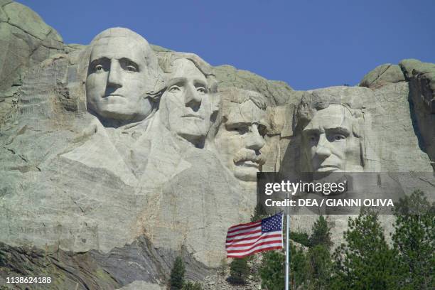 The faces of American Presidents George Washington, Thomas Jefferson, Theodore Roosevelt e Abraham Lincoln carved in the granite, American flag in...