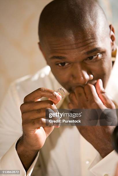 young man nervously holding and looking at an engagement ring - men rings stock pictures, royalty-free photos & images