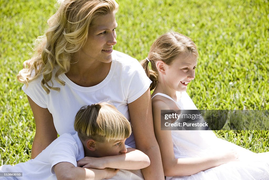 Mother sitting on grassy front lawn with her son and daughter