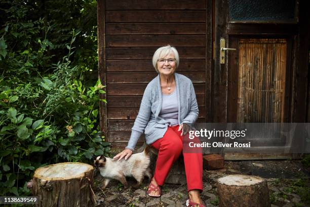 smiling senior woman sitting at garden shed stroking a cat - old lady cat stock pictures, royalty-free photos & images