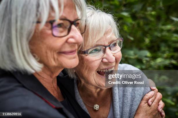 two senior women hugging in garden - senior adult friends stock pictures, royalty-free photos & images