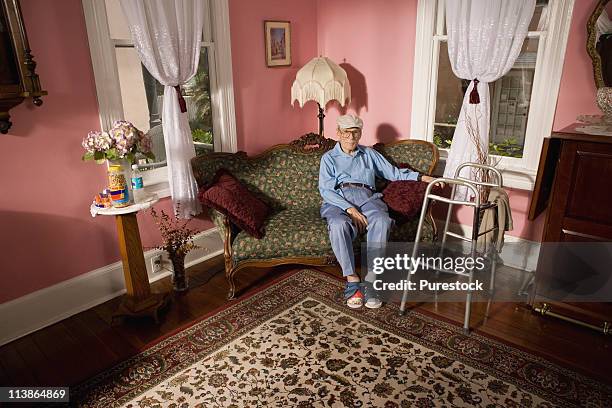 senior man sitting on sofa in living room - einzelner senior stock-fotos und bilder
