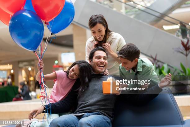 gelukkige familie verrassende vader met een cadeau in een winkelcentrum - family mall stockfoto's en -beelden