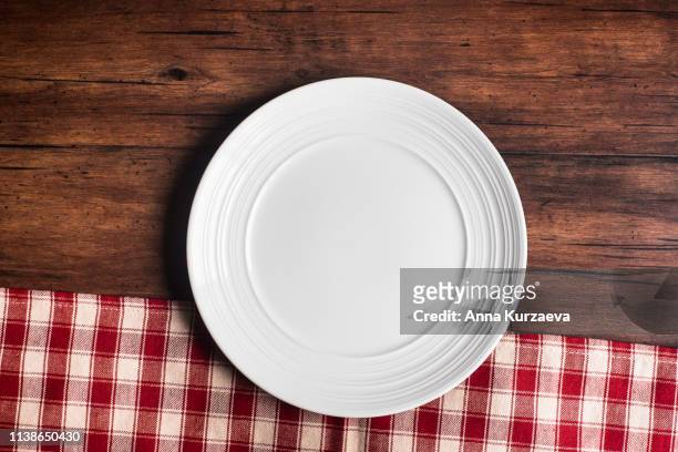 empty white plate on a napkin on an old wooden brown background, top view. image with copy space. kitchen table with a towel and a plate - top view with copy space. - clean wood table stock-fotos und bilder