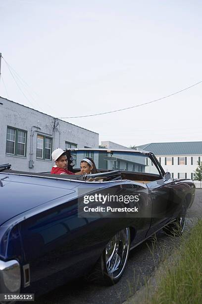 portrait of a young hip-hop couple sitting in a pimped-up vintage car in urban neighborhood - pimped car foto e immagini stock