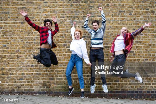 gruppe von teenagern springt gegen eine ziegelwand - jumping girl stock-fotos und bilder